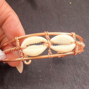 May include: A copper wire bracelet with two white cowrie shells woven into the design.