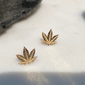 May include: A pair of gold-toned earrings shaped like marijuana leaves.
