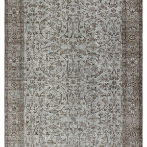 May include: Rectangular area rug with a faded, vintage appearance. The rug features a central field of light gray with a repeating floral pattern in brown. A darker brown border frames the design.