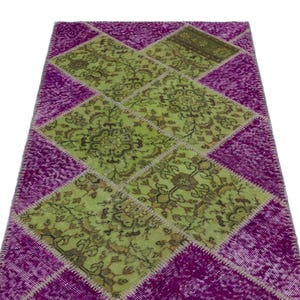 Puede incluir: Una alfombra rectangular de patchwork con un diseño vibrante. La alfombra presenta una combinación de tonos verde lima y morado intenso, con patrones en forma de diamante. Las secciones verdes muestran intrincados motivos florales, mientras que las secciones moradas tienen una apariencia texturizada.