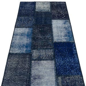 May include: A rectangular patchwork rug in shades of blue. The rug is made up of various rectangular patches of different blue hues, creating a textured and visually interesting pattern. The rug appears to be made of a soft material.