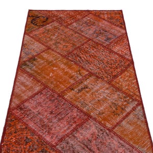 May include: A rectangular, patchwork rug with a diamond pattern. The rug features a variety of warm colors, including shades of red, orange, and peach. The rug's design is made up of numerous geometric shapes, creating a textured appearance.