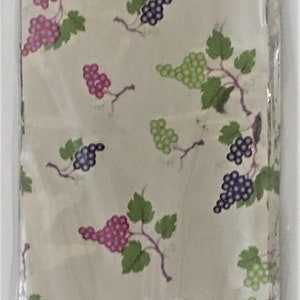 Puede incluir: Una pila de servilletas de tela blancas con un patr&oacute;n repetido de vides verdes y uvas moradas y rosadas.