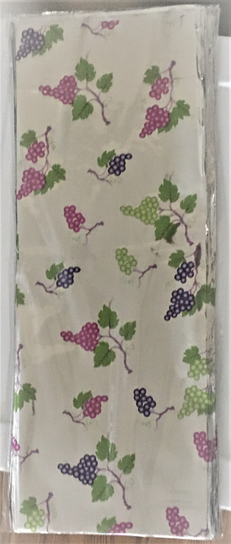 Puede incluir: Una pila de servilletas de tela blancas con un patr&oacute;n repetido de vides verdes y uvas moradas y rosadas.