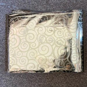 May include: A silver emergency blanket with a white swirl pattern. The blanket is folded and appears to be made of a thin, reflective material.