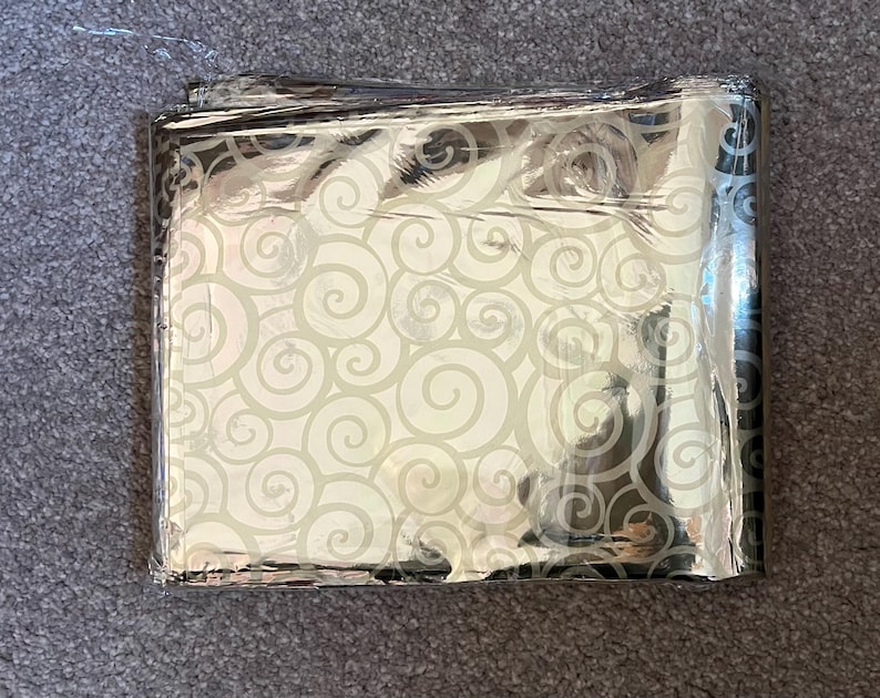 May include: A silver emergency blanket with a white swirl pattern. The blanket is folded and appears to be made of a thin, reflective material.