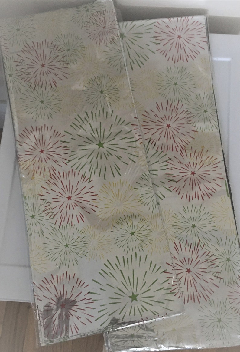 Puede incluir: Dos rollos de papel de regalo blanco con un patr&oacute;n de fuegos artificiales rojo, verde y amarillo.