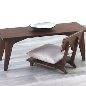May include: A dark brown wooden table with a white ceramic bowl on top. A dark brown wooden chair with a light gray cushion is next to the table.