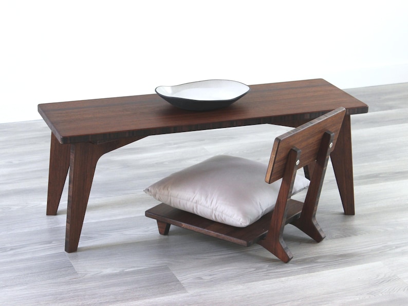 May include: A dark brown wooden table with a white ceramic bowl on top. A dark brown wooden chair with a light gray cushion is next to the table.