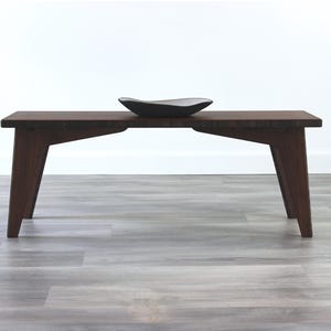 May include: A dark brown wooden bench with a simple design and angled legs. A black ceramic bowl sits on top of the bench.