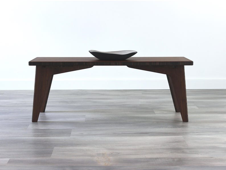 May include: A dark brown wooden bench with a simple design and angled legs. A black ceramic bowl sits on top of the bench.