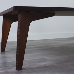 May include: A dark brown wooden coffee table with a rectangular top and four angled legs. The table is made of wood with a natural grain pattern.