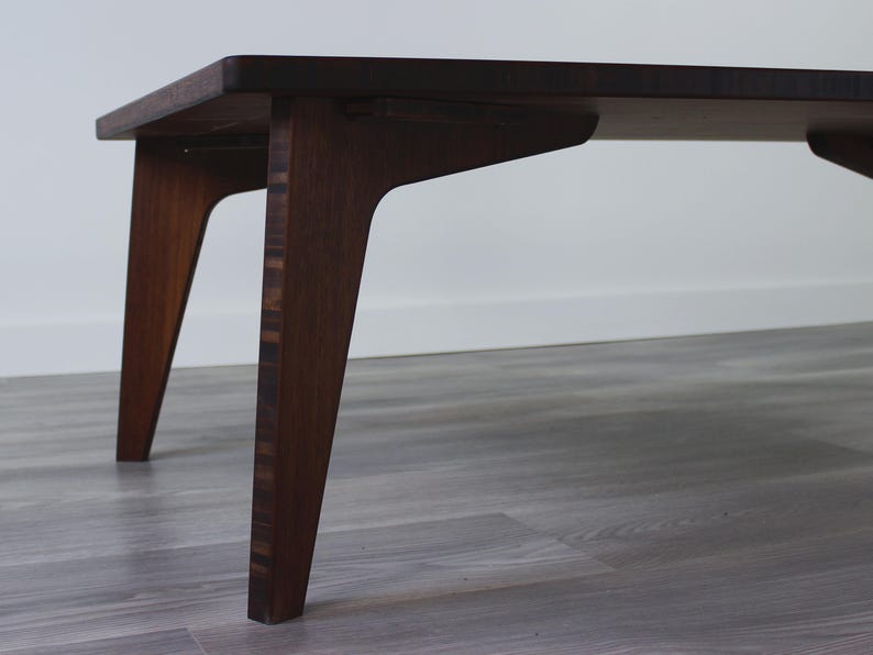 May include: A dark brown wooden coffee table with a rectangular top and four angled legs. The table is made of wood with a natural grain pattern.
