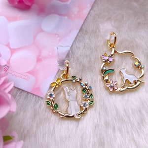 Peut inclure: Deux breloques dorées représentant un chat blanc dans une couronne de fleurs. Les breloques ont un design délicat avec des accents d'émail colorés et des strass. Les breloques sont parfaites pour ajouter une touche de fantaisie à des bijoux ou des objets artisanaux.