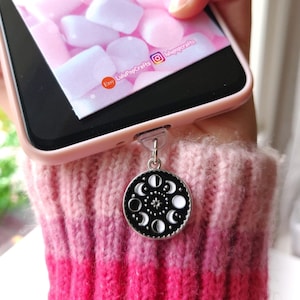 Può includere: Un ciondolo per telefono argentato con un design a fasi lunari in bianco e nero. Il ciondolo è attaccato a una custodia per telefono rosa. Il telefono mostra un'immagine rosa e bianca con il testo "LuluPop Crafts".
