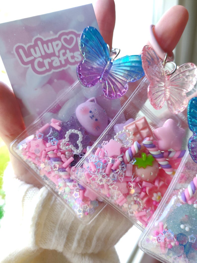May include: Clear rectangular resin keychains filled with pink and purple confetti, stars, and small charms. Each keychain features a colorful butterfly on top. The keychains are decorated with a variety of cute, colorful charms and the text "Lulup Crafts".