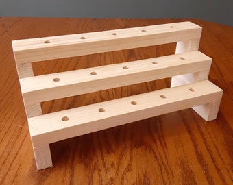 Può includere: Un espositore in legno a tre livelli con più fori per esporre oggetti. L'espositore è realizzato in legno naturale e ha un aspetto rustico.