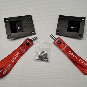 May include: A set of black square mounting plates with four screw holes, two red fabric pull straps with "OPEN DOOR" text, and a small bag of screws. The items are arranged on a white surface.