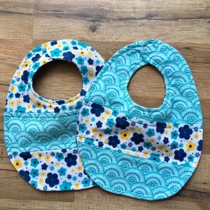May include: Two baby bibs with a blue and white floral pattern and a blue and white wave pattern. The bibs are made of soft cotton and are perfect for keeping baby's clothes clean.
