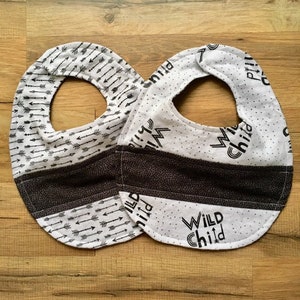 May include: Two black and white baby bibs. One bib has a black and white arrow pattern and the other has the text "WILD CHILD" in black on a white background.