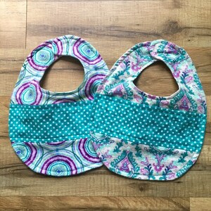 May include: Two baby bibs with a turquoise and white polka dot pattern in the center. The bibs are made of a soft, absorbent fabric and feature a unique, colorful design.