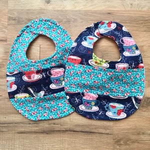 May include: Two baby bibs with a teal and navy blue fabric featuring a teacup pattern. The bibs are made of soft, absorbent fabric and are perfect for keeping baby's clothes clean.