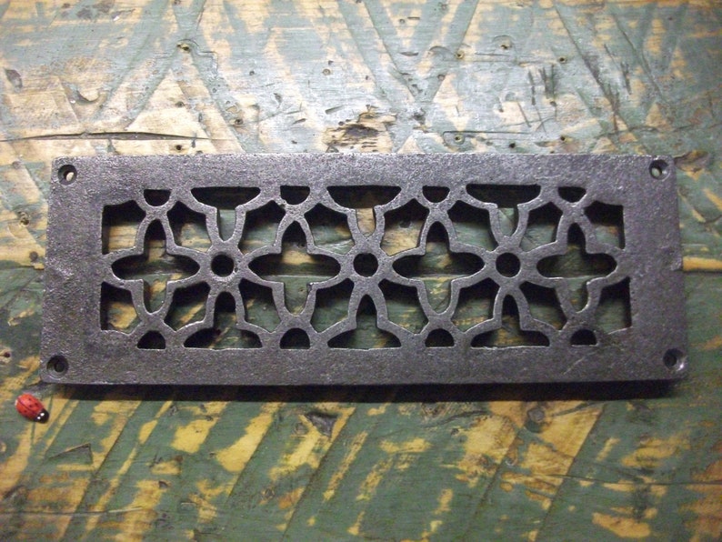 May include: A rectangular cast iron vent cover with a decorative floral pattern. The vent cover is dark gray and has a slightly distressed finish.