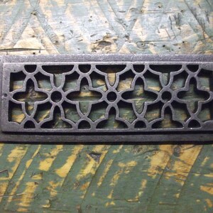 May include: A rectangular cast iron vent cover with a decorative floral pattern. The vent cover is dark gray and has a slightly distressed finish.