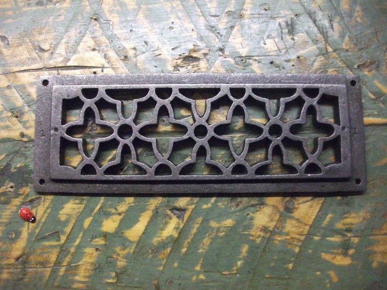 May include: A rectangular cast iron vent cover with a decorative floral pattern. The vent cover is dark gray and has a slightly distressed finish.