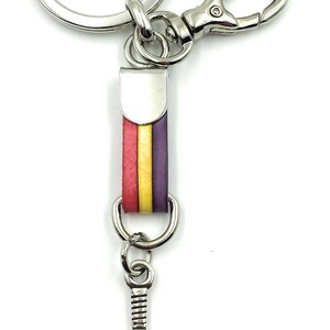 May include: A silver key chain with a red, yellow, and purple striped leather charm. The charm is attached to a silver paddle shaped charm with a small hole in the center.