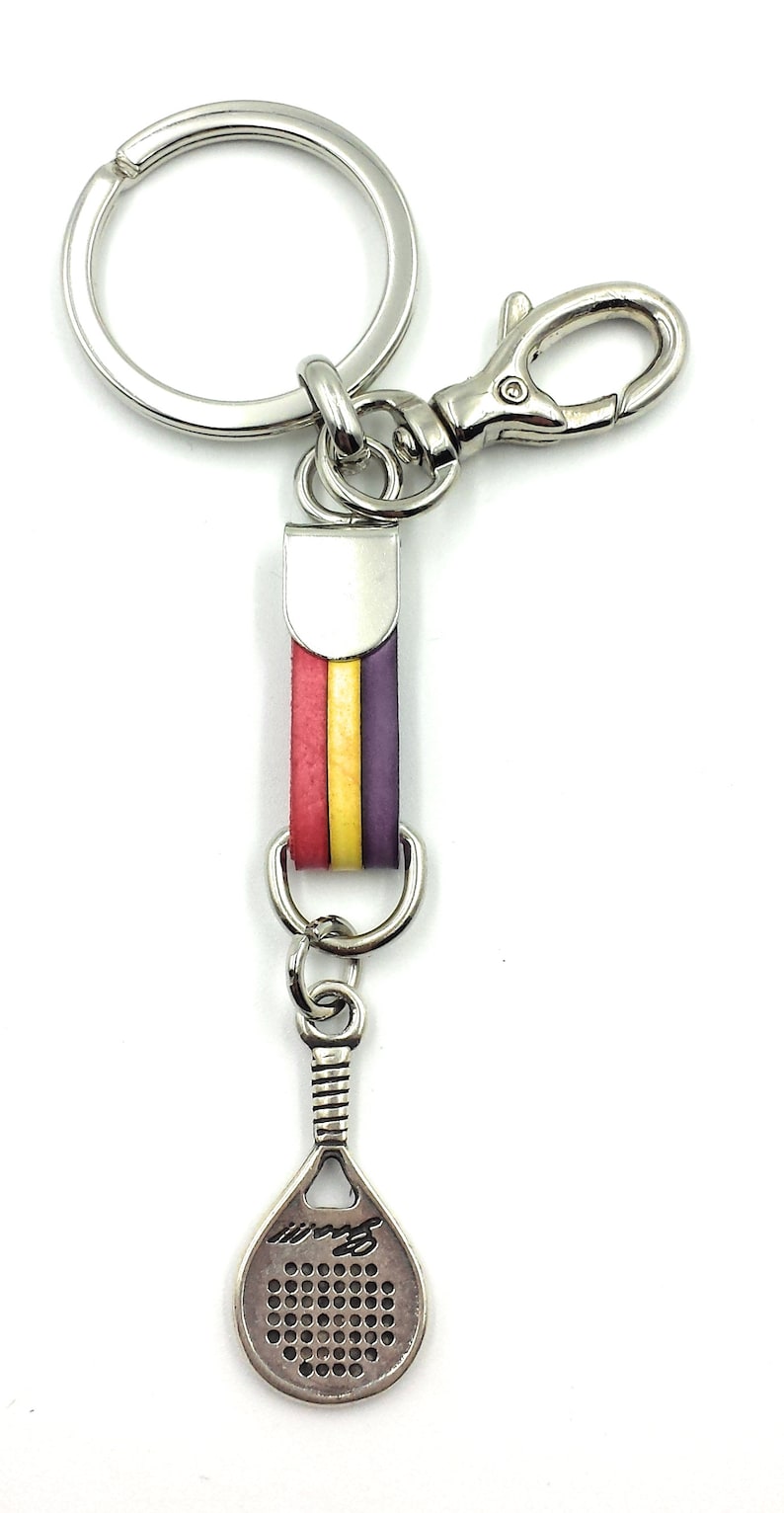 May include: A silver key chain with a red, yellow, and purple striped leather charm. The charm is attached to a silver paddle shaped charm with a small hole in the center.