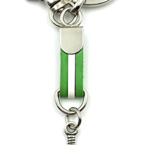 May include: A silver key chain with a green leather strap and a silver paddle shaped charm. The charm has a grid pattern and the word "padel" written on it.