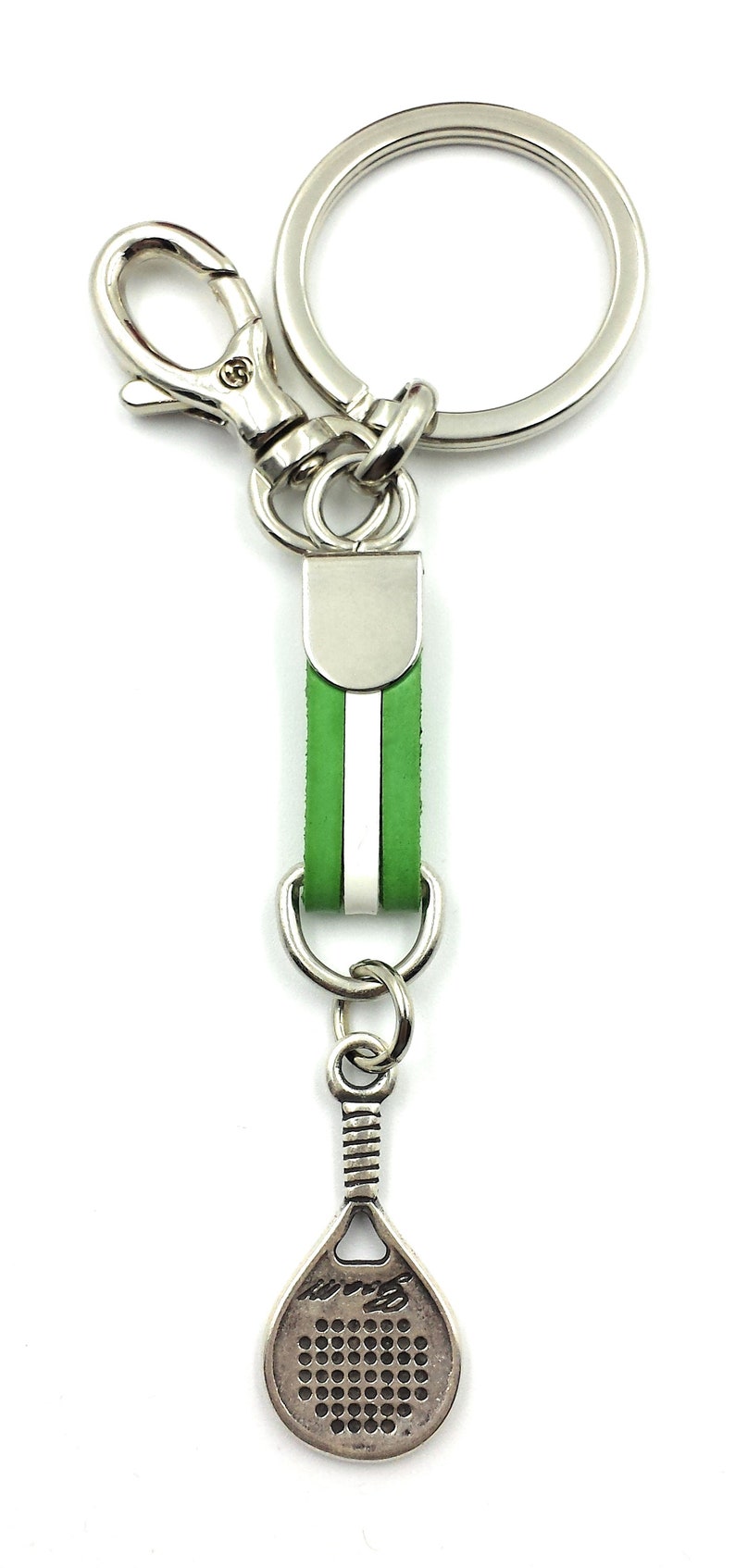May include: A silver key chain with a green leather strap and a silver paddle shaped charm. The charm has a grid pattern and the word "padel" written on it.