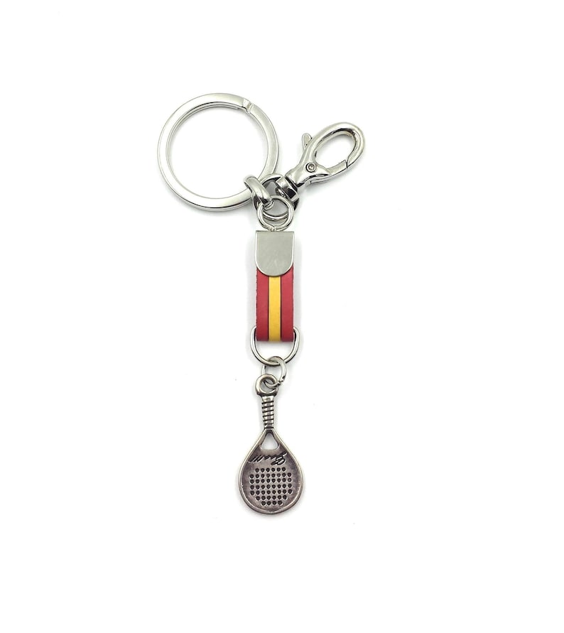May include: A silver key chain with a red and yellow leather strap and a silver padel racket charm.