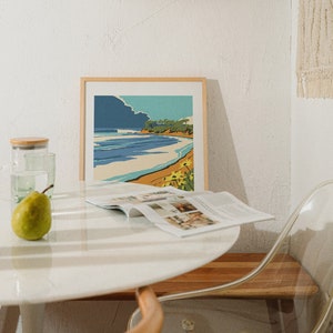 May include: A white table with a magazine, a green pear, and a glass of water. A framed print of a beach scene hangs on the wall above the table. A clear plastic chair sits next to the table.