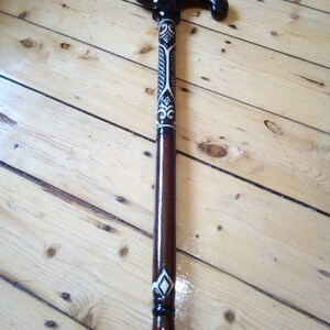 May include: A wooden walking stick with a black and white patterned handle. The handle is curved and has a decorative design.