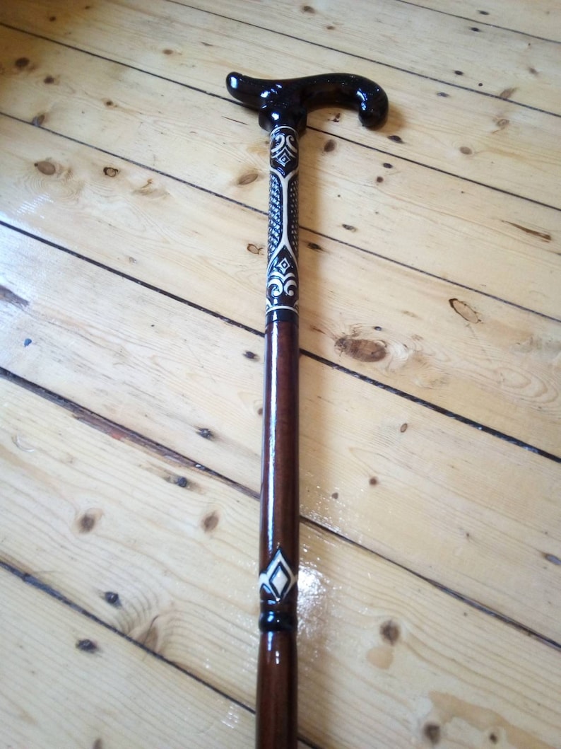 May include: A wooden walking stick with a black and white patterned handle. The handle is curved and has a decorative design.