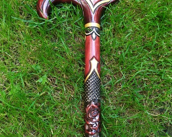 May include: A wooden walking stick with a carved rose design and gold accents. The stick is painted red and black.