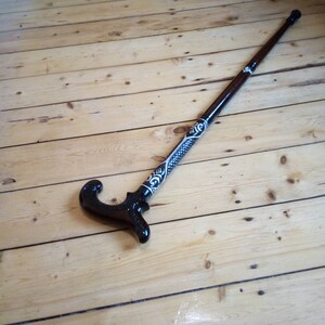 May include: A wooden walking stick with a black and white patterned design. The handle is curved and has a decorative design.