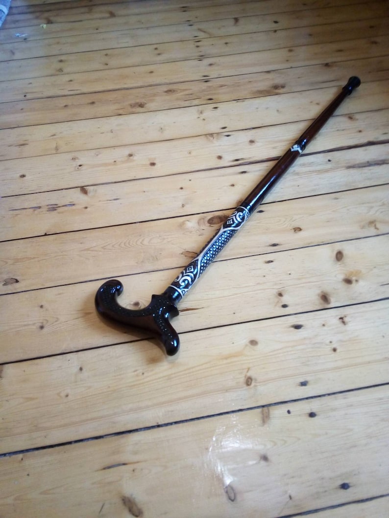 May include: A wooden walking stick with a black and white patterned design. The handle is curved and has a decorative design.