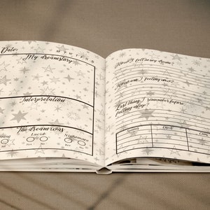 May include: A white journal with a star pattern on the cover. The journal is open to a page with the title "My Dreamstory" and a section for recording dreams and interpretations. The page also includes a section for recording the time of day, the day of the week, and whether the dream was recurring, lucid, or a nightmare.