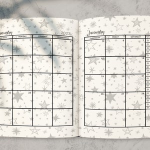 May include: A white planner with a black grid and a star pattern. The planner is open to January 2023. The days of the week are labeled at the top of each column. There is a notes section on the right side of the planner.