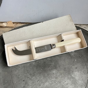 May include: A white handled cheese knife in its original box. The knife has a silver blade with the inscription "GRUBB & CO LTD SHEFFIELD ENGLAND" and a small logo.