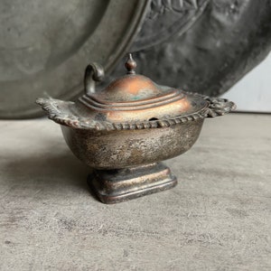 May include: A silver and copper colored metal salt cellar with a lid and a decorative base. The salt cellar has a small hole in the lid for pouring.