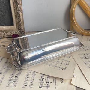 May include: A silver serving dish with a lid and two handles. The dish is sitting on a sheet of music.