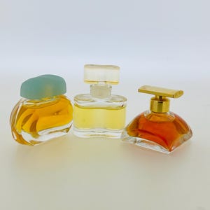 May include: Three glass perfume bottles with different coloured liquids. The bottle on the left has a light blue cap, the middle bottle has a clear cap, and the bottle on the right has a gold cap.