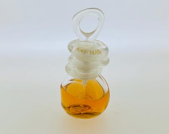 May include: A clear glass bottle of perfume with a gold liquid inside. The bottle has a clear plastic stopper with a ring handle and the word "NAF NAF" printed on it.