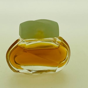 May include: A small, clear glass perfume bottle with a light green cap. The bottle contains a golden-coloured liquid. The bottle has a rounded, asymmetrical shape.