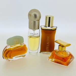 May include: Four bottles of perfume, two with gold caps, one with a green cap, and one with a clear cap. The bottles are filled with a light amber liquid. The bottles are labelled "Estee Lauder" and "Est&eacute;e Lauder Pleasures".