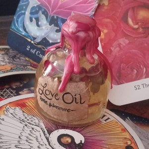 May include: A small glass bottle with a pink wax seal, filled with a clear liquid. The bottle has a label that reads "Love Oil Rose & Jasmine".